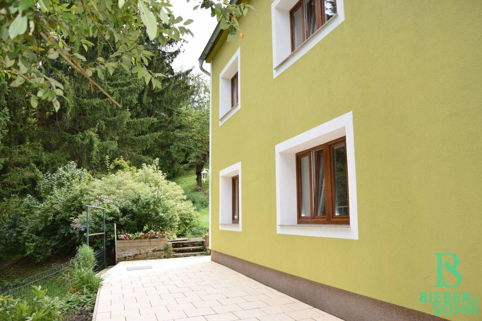 Gepflasterte Terrasse neben dem Haus mit Blick auf die grüne Umgebung.