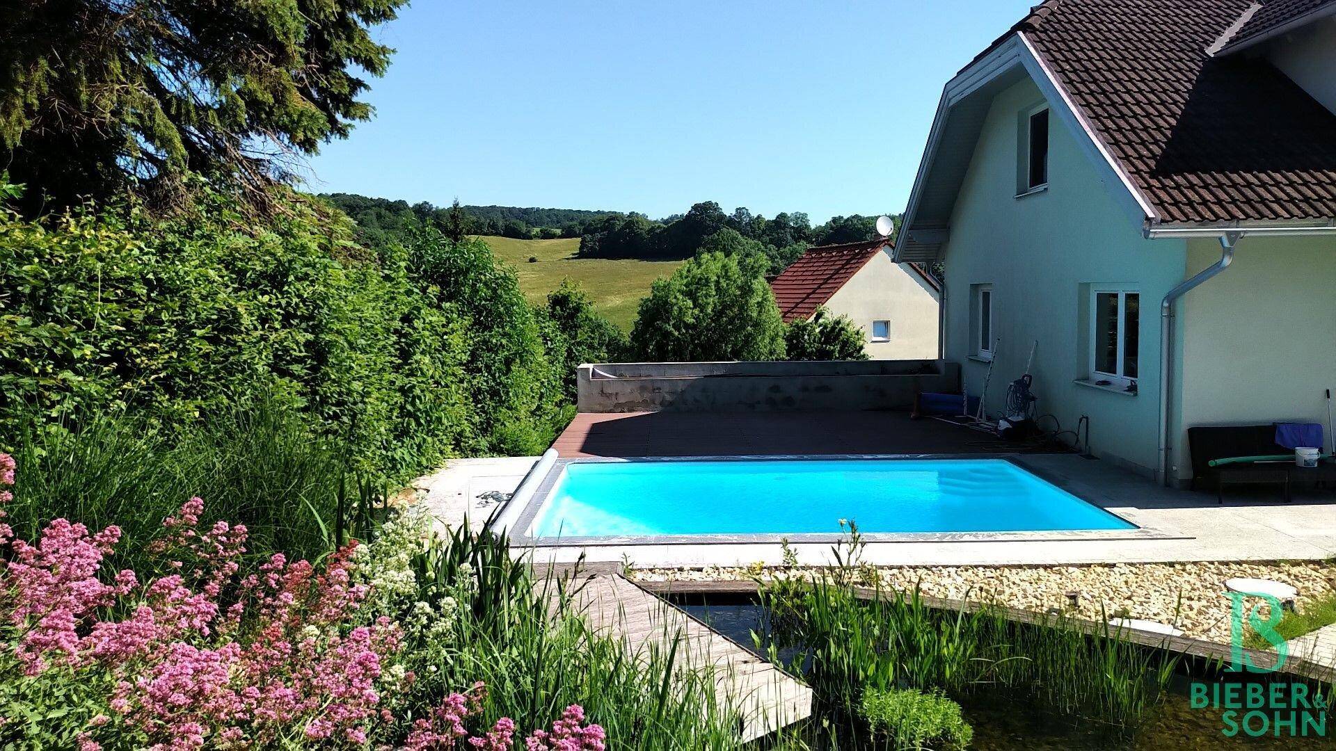 Außenbereich mit Pool und weitem Blick über die grüne Landschaft und umliegende Häuser.