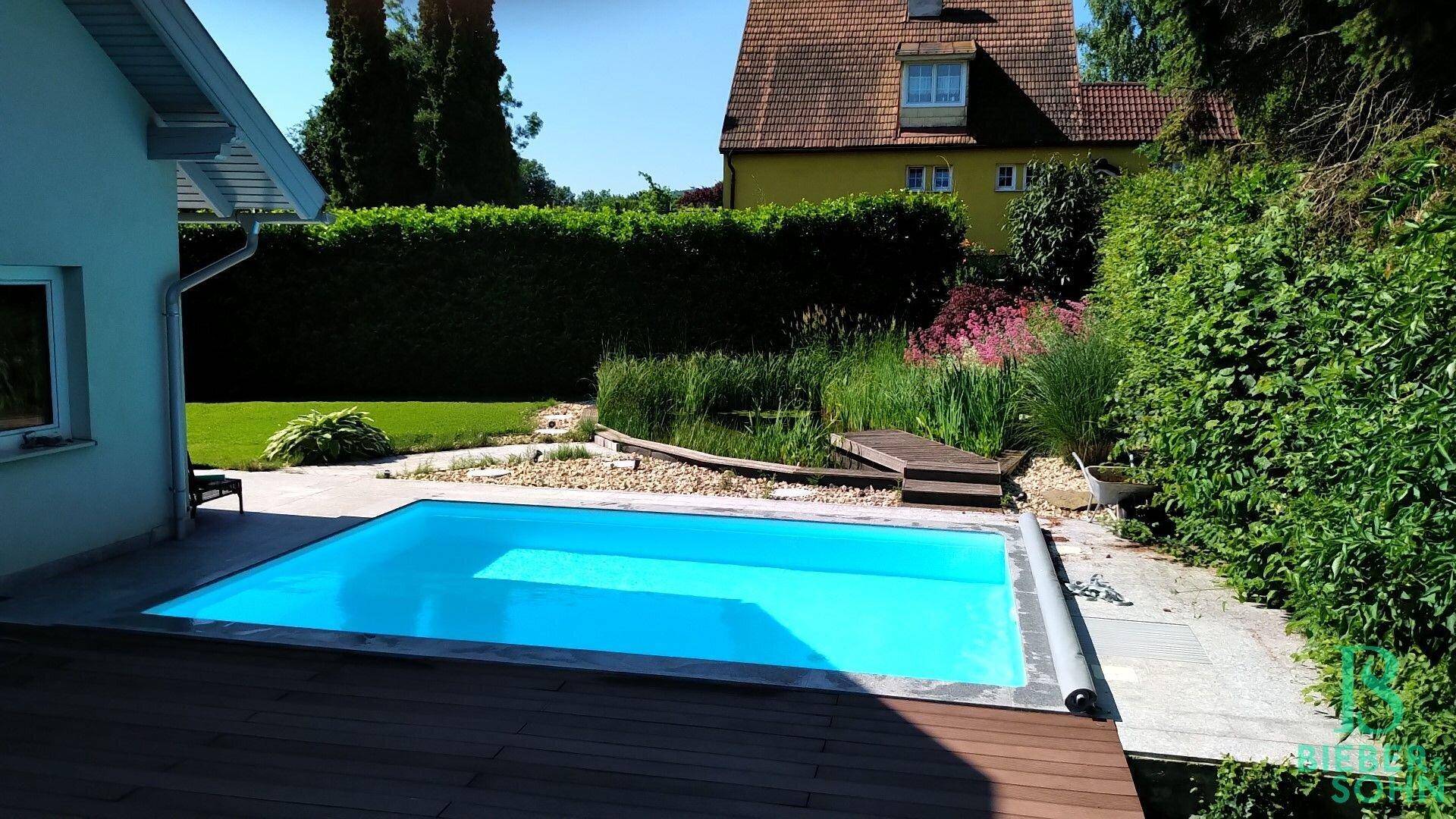 Gepflegter Poolbereich mit Holzdeck und Blick auf das Nachbarhaus und den Garten.