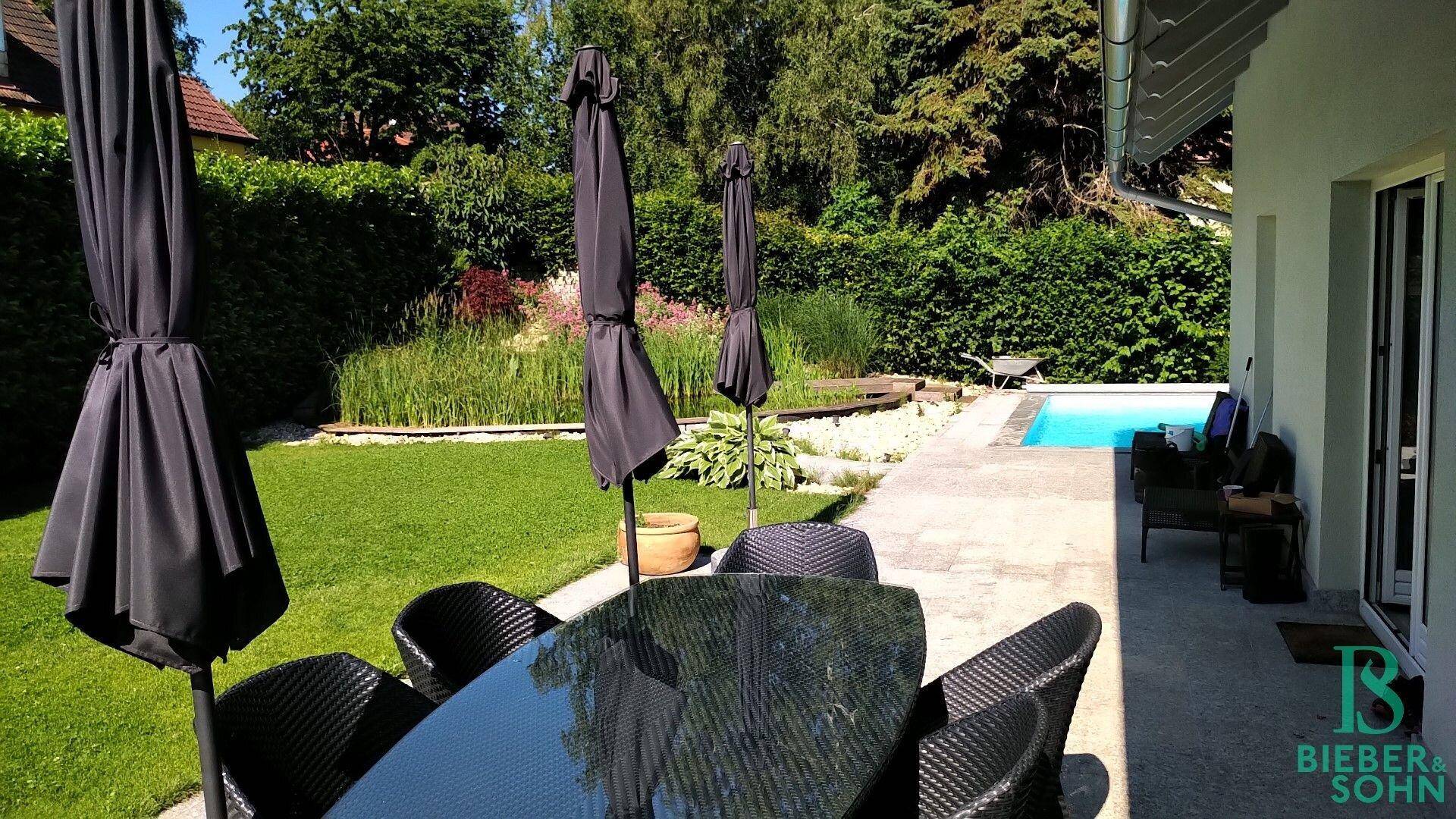 Geräumige Terrasse mit Gartenmöbeln und Sonnenschirmen, angrenzend an den Rasen und Pool.