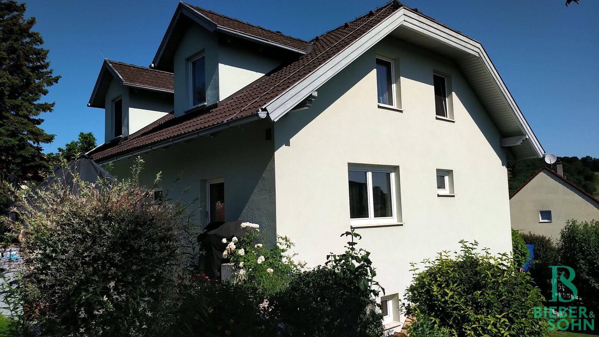 Ansicht des Einfamilienhauses mit heller Fassade, Satteldach und mehreren Fenstern.