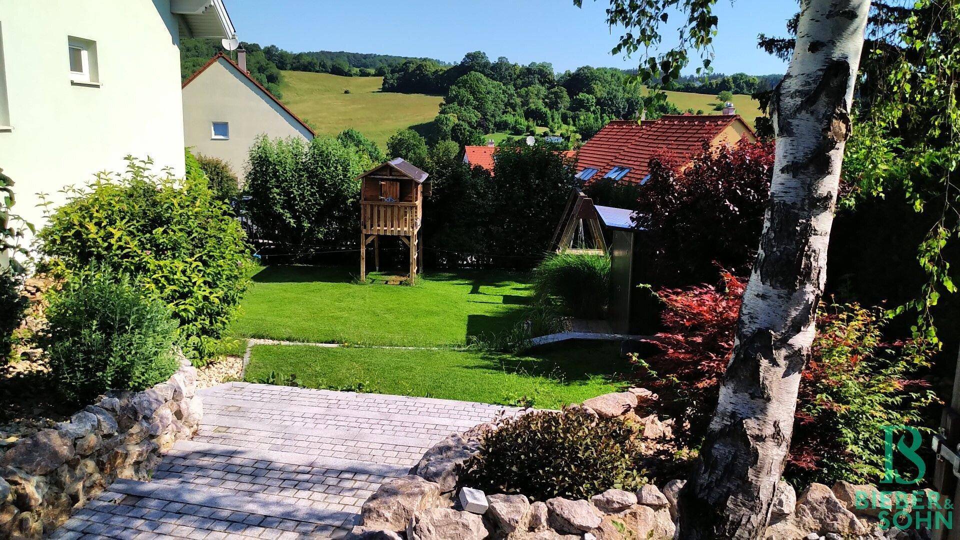 Garten mit Spielhaus und Blick auf die umliegende grüne Landschaft und Häuser.