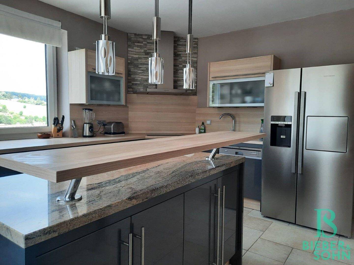 Helle Küche mit Kücheninsel, modernen Geräten und Holz- sowie Granitarbeitsplatten.