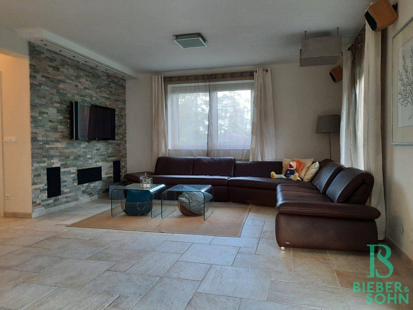 Helles Wohnzimmer mit großem Ecksofa, Fliesenboden und dekorativer Steinwand.