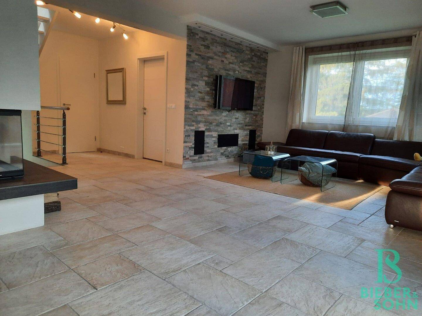 Geräumiges Wohnzimmer mit Fliesenboden, Kamin und Zugang zu anderen Bereichen.