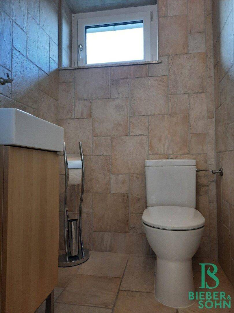 Gäste-WC mit beigefarbenen Fliesen, modernem Waschbecken und Fenster.