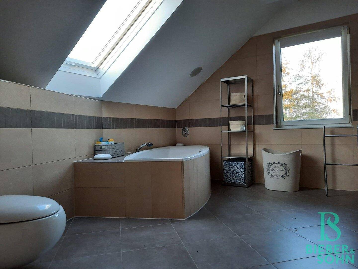 Badezimmer im Dachgeschoss mit Badewanne, Dachfenster und beigefarbenen Fliesen.