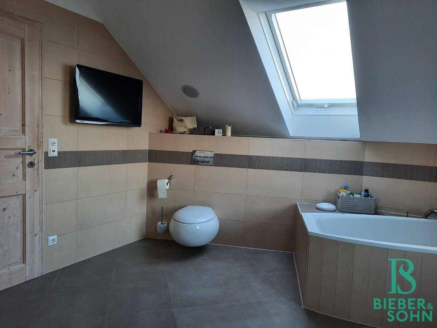 Geräumiges Badezimmer mit Badewanne, Wand-WC und Dachfenster für natürliches Licht.
