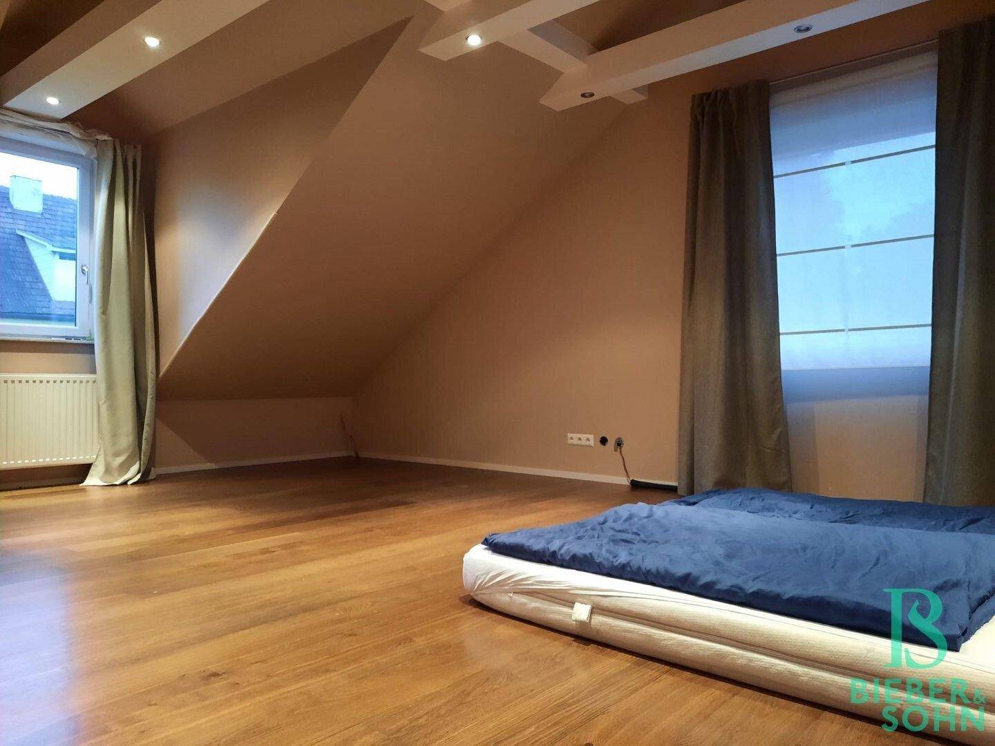 Geräumiges Schlafzimmer im Dachgeschoss mit Holzboden, Dachschrägen und Einbaustrahlern.