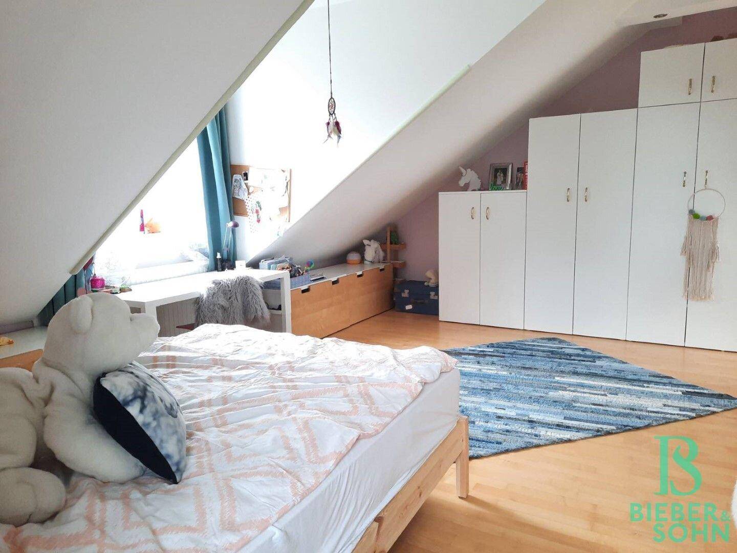 Kinderzimmer im Dachgeschoss mit Holzboden, Dachschrägen und großem Kleiderschrank.