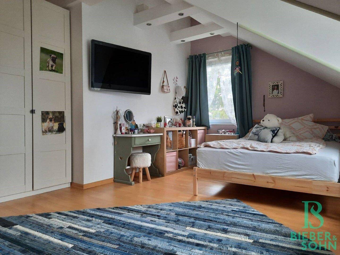 Helles Kinderzimmer im Dachgeschoss mit Holzboden, Dachschrägen und TV-Gerät.