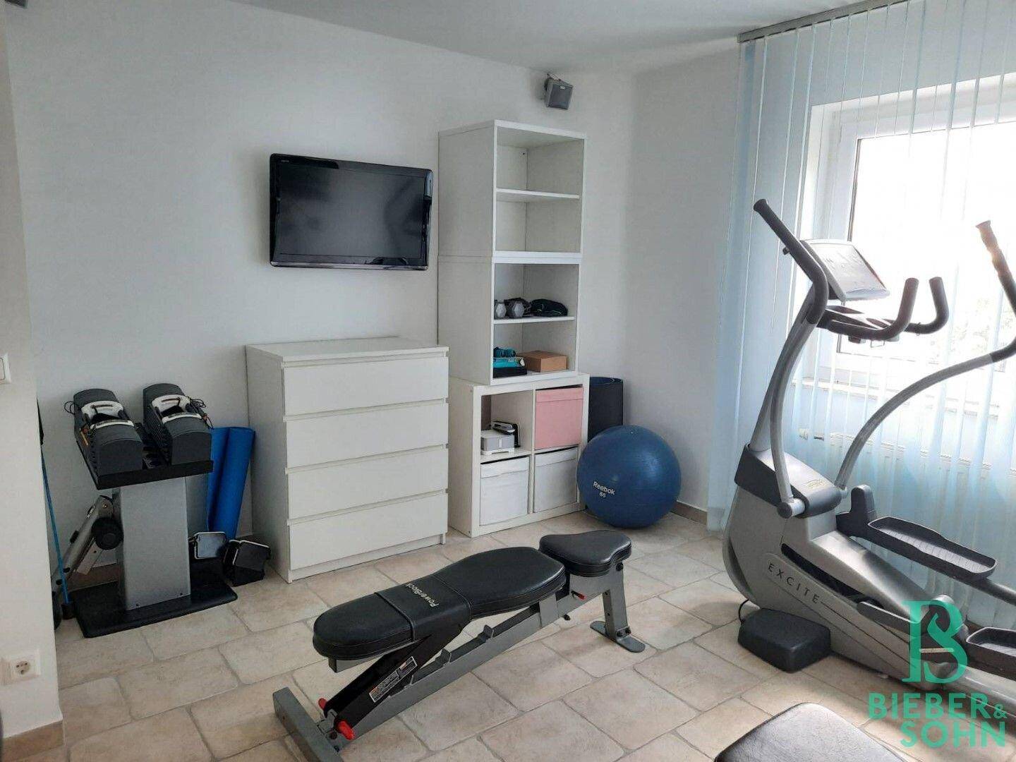 Fitnessraum mit Trainingsbank, Crosstrainer und Regalen für Sportzubehör.