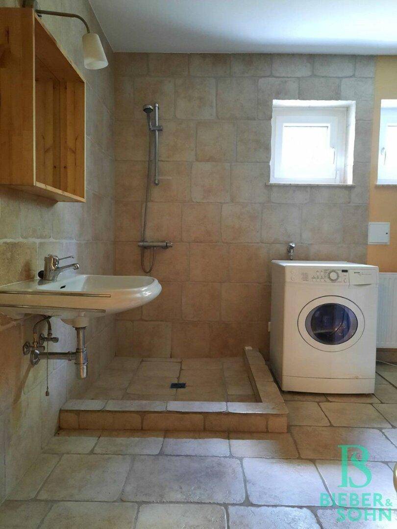 Badezimmer mit Dusche, Waschbecken und Waschmaschine, ideal als Hauswirtschaftsraum.