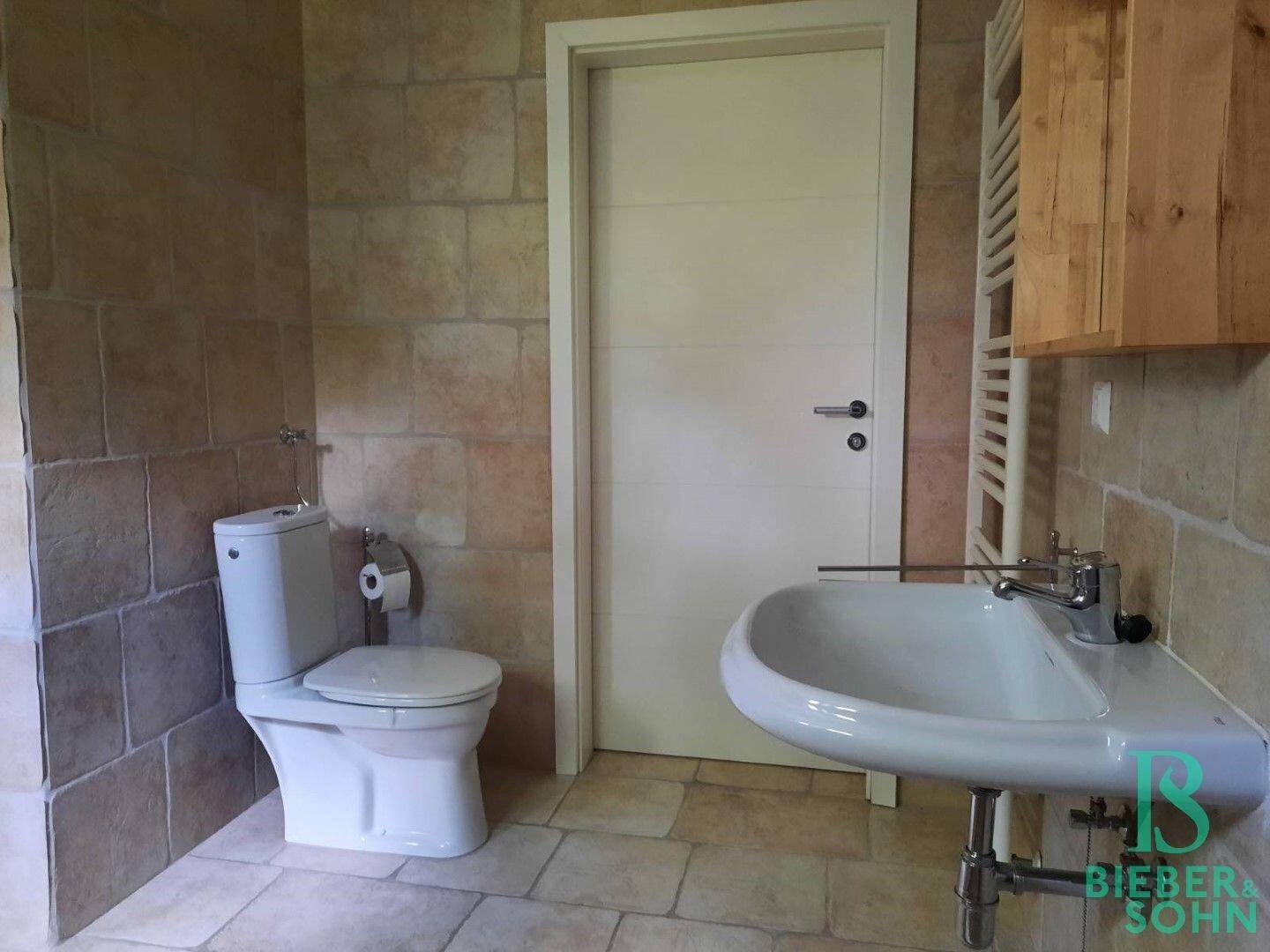 Badezimmer mit WC, Waschbecken und beheiztem Handtuchhalter, gefliest in warmen Tönen.