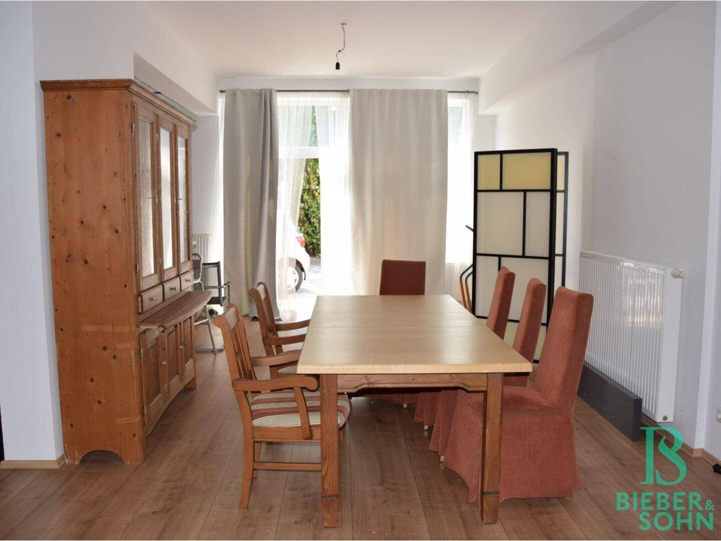 Heller Essbereich mit Holztisch, Stühlen und einem traditionellen Holzschrank, mit Blick nach draußen.