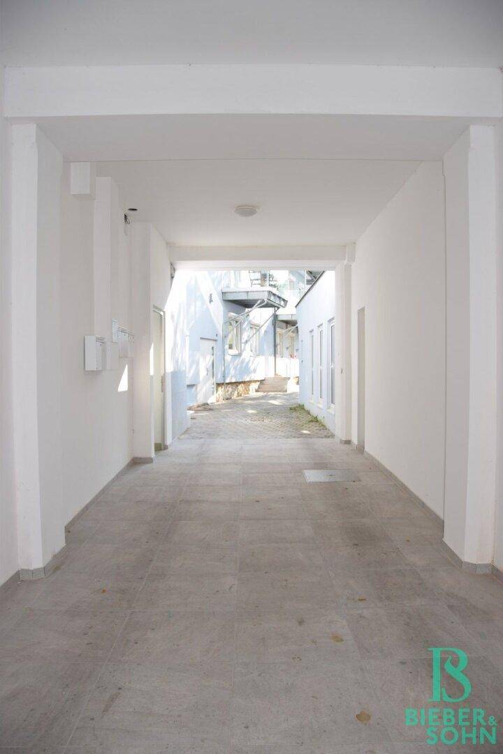 Überdachter Eingangsbereich mit gefliestem Boden und Zugang zu weiteren Gebäudeteilen.