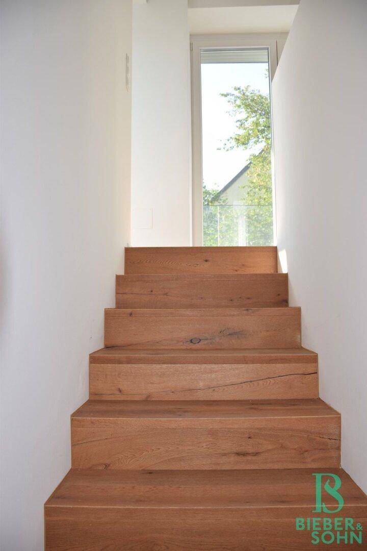 Moderne Holztreppe mit natürlichem Lichteinfall durch ein hohes Fenster.