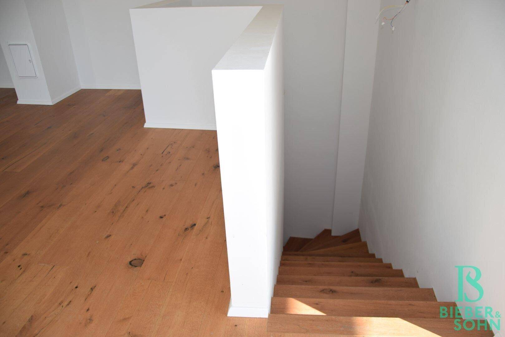 Moderner Treppenabgang mit Holzdielen und weißer Wand, die in den unteren Bereich führt.