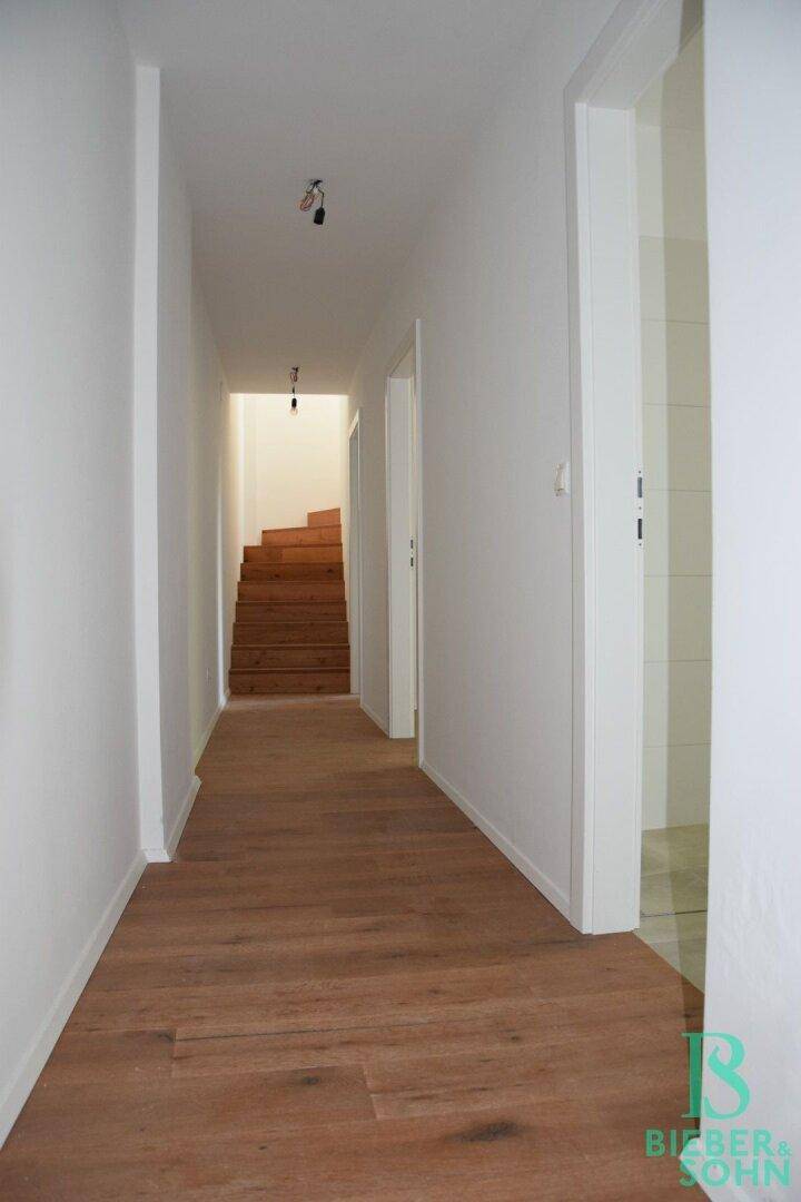 Heller Flur mit Holzboden und Türen, der zu weiteren Räumen und einer Treppe führt.