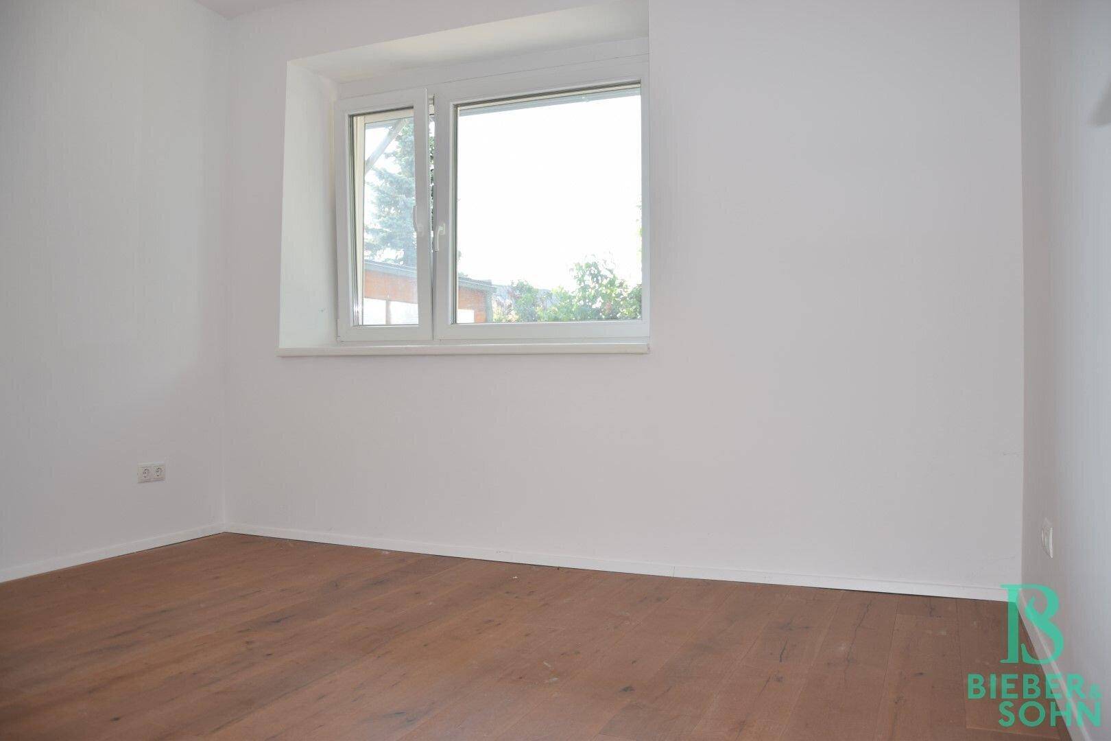 Helles Schlafzimmer mit Holzboden und einem Fenster, das den Blick ins Grüne freigibt.