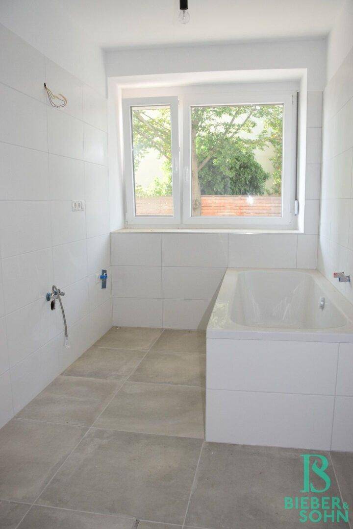 Modernes Badezimmer mit Badewanne, weißen Fliesen und einem Fenster für Tageslicht.