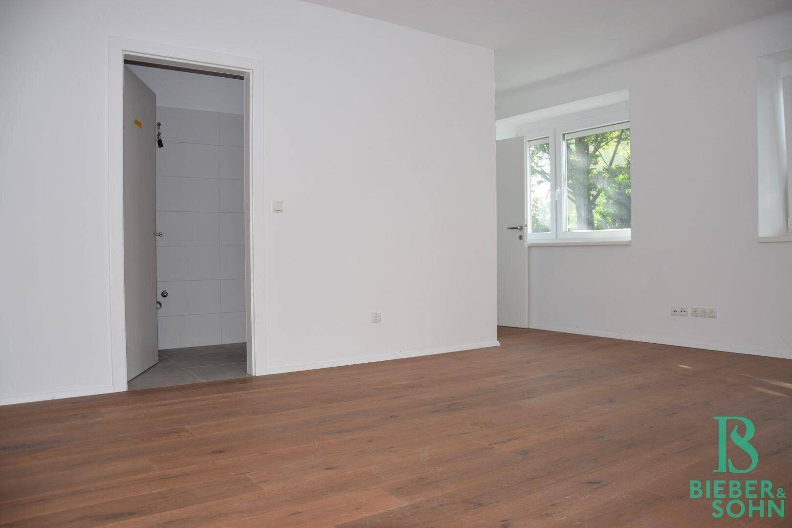 Helles Zimmer mit Holzboden und Zugang zu einem weiteren Raum, ideal als Schlafzimmer.