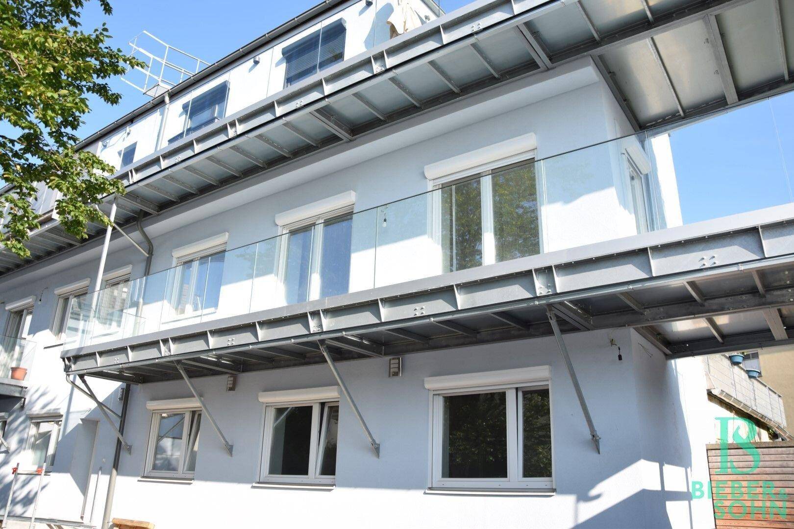 Moderne Gebäudefassade mit mehreren Balkonen und großen Fenstern unter blauem Himmel.