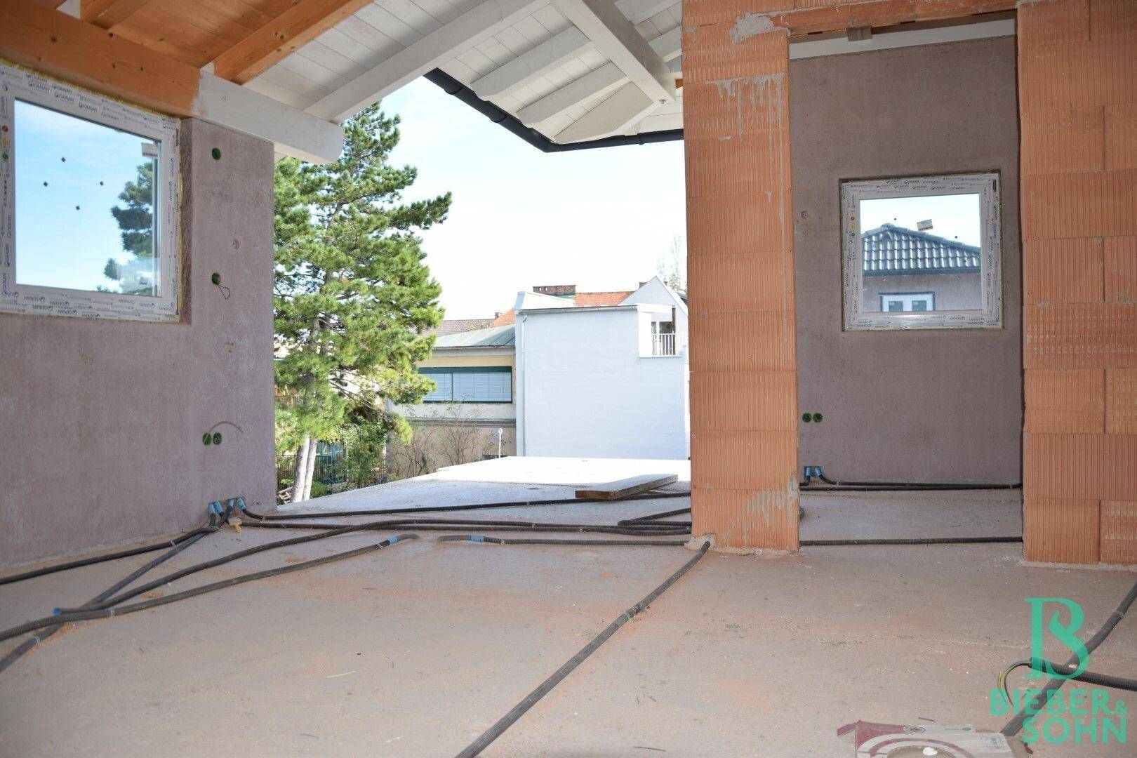 Unfertiger Innenraum im Rohbau mit Blick ins Freie und sichtbaren Installationen.