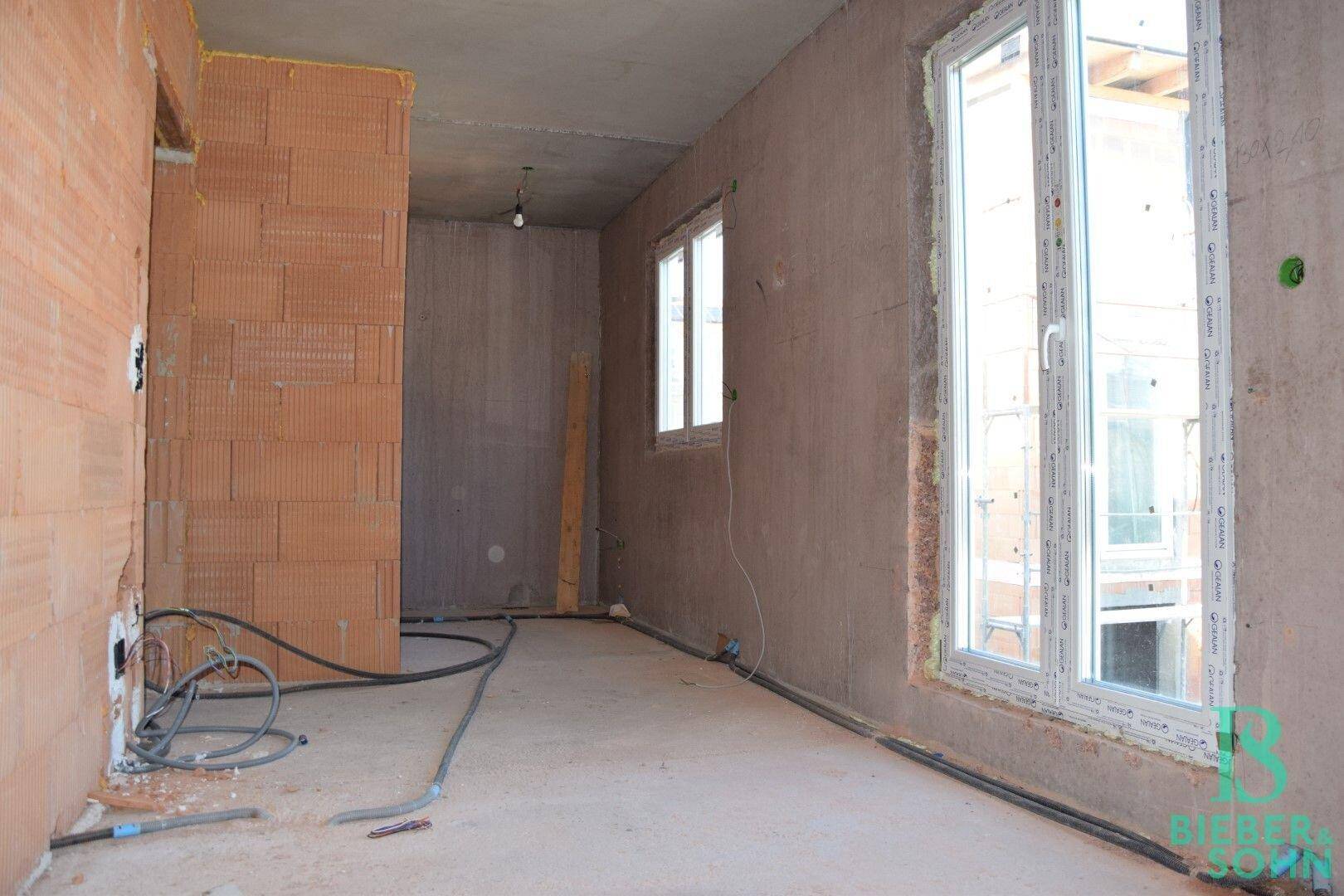 Rohbau-Innenraum mit großen Fenstern, die viel Tageslicht hereinlassen.