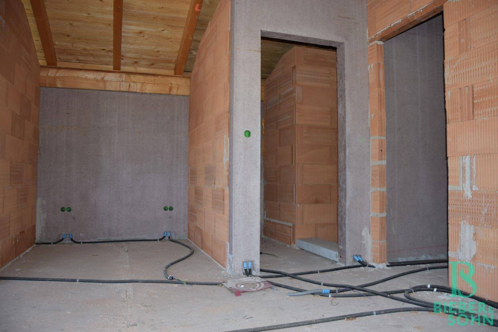 Rohbau-Innenraum mit Ziegelwänden, Holzdecke und vorbereiteten Türöffnungen.