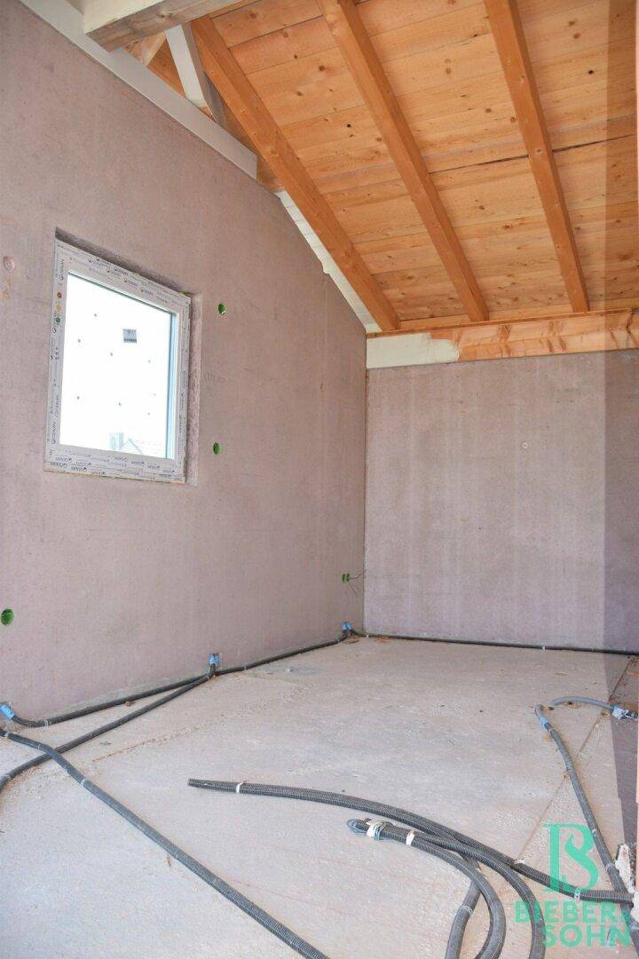 Unfertiger Raum im Dachgeschoss mit Fenster, Holzdecke und sichtbaren Installationen.