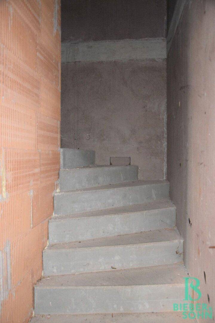 Unfertige Betontreppe in einem Rohbau mit Ziegelwänden, die in ein Obergeschoss führt.