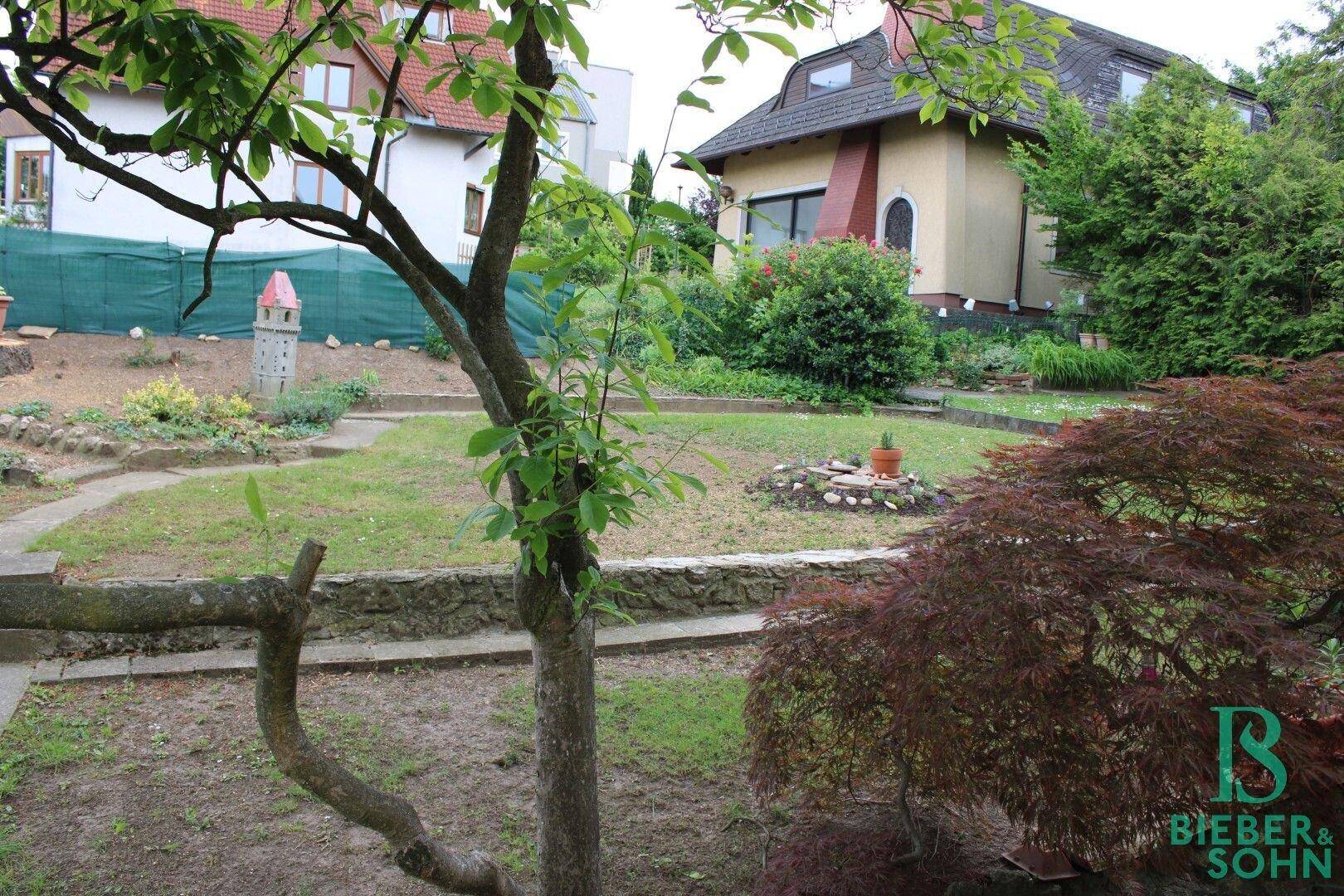 Großer Garten mit Rasenfläche, Bäumen und einem kleinen Gartenhäuschen im Hintergrund.