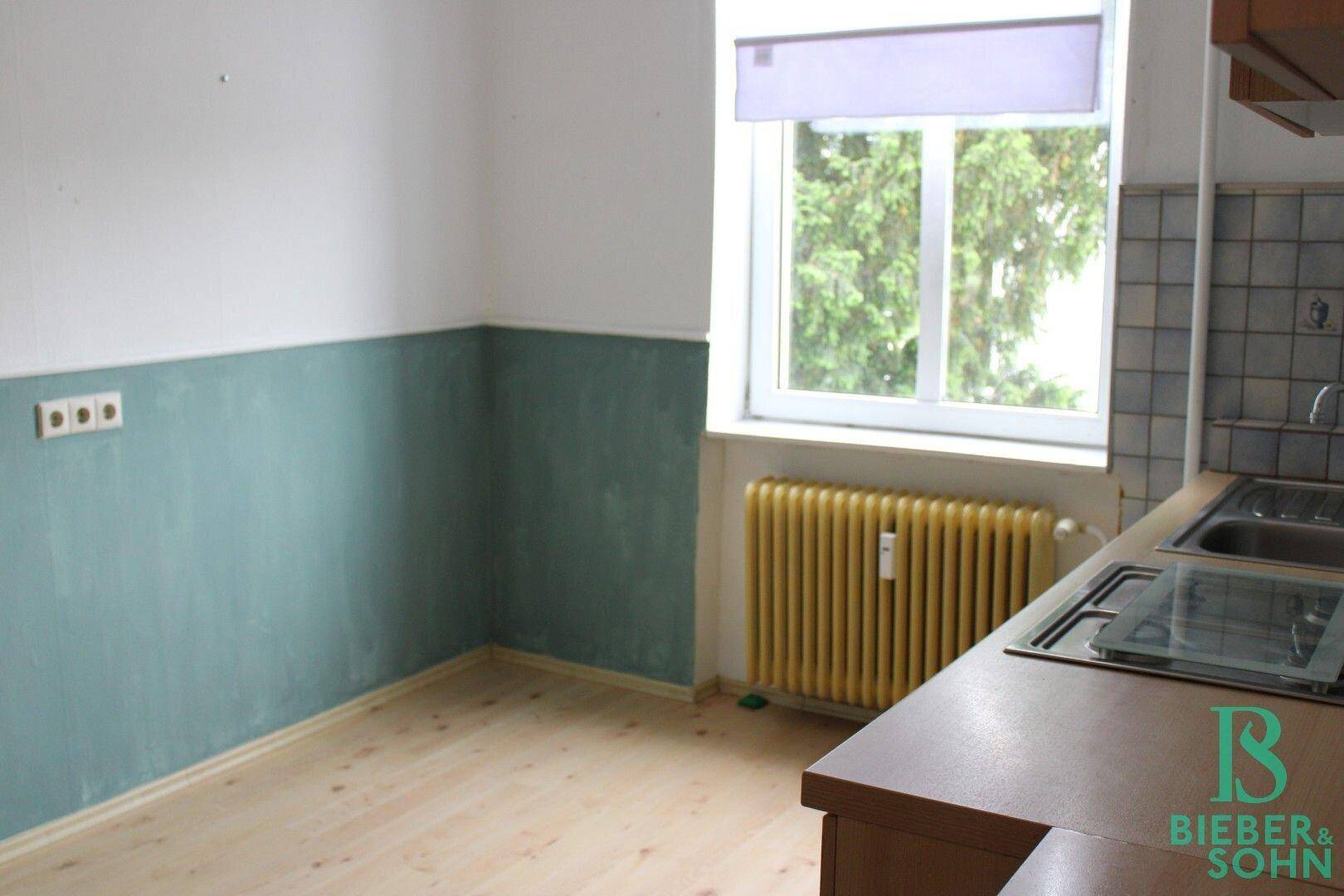 Helle Küche mit Holzboden, zweifarbigen Wänden und einem Fenster mit Blick ins Grüne.