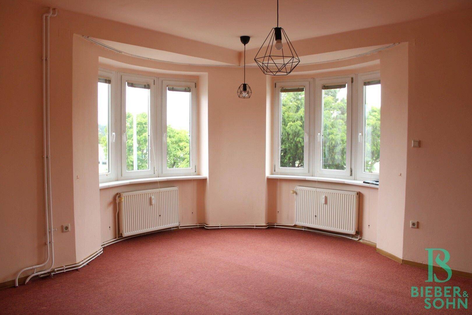 Geräumiges Zimmer mit Erkerfenstern, Teppichboden und Blick ins Grüne.