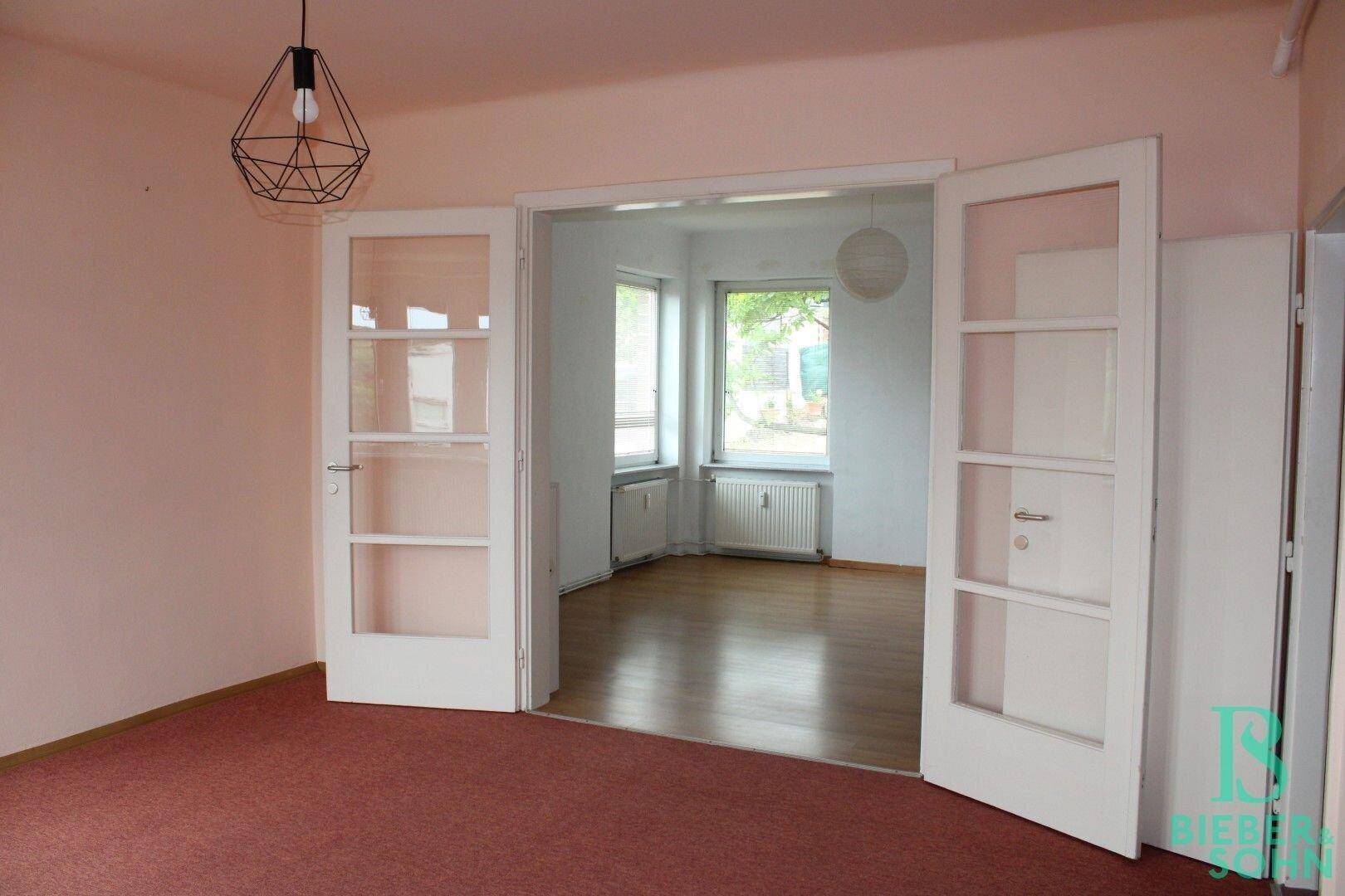 Zwei miteinander verbundene Zimmer mit Teppichboden und Holztüren mit Glaseinsätzen.