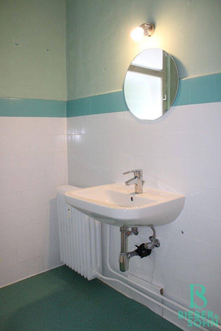 Badezimmer mit Waschbecken, Spiegel und weiß-türkisen Fliesen.