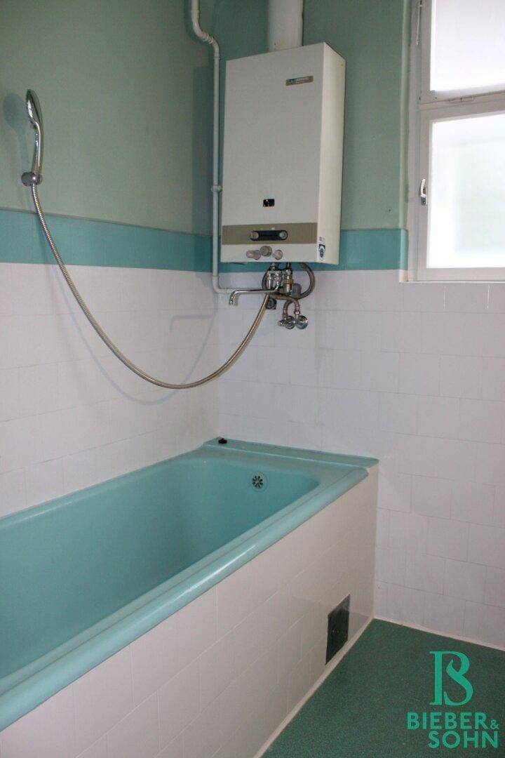 Badezimmer mit Badewanne, Gastherme und weiß-türkisen Fliesen.