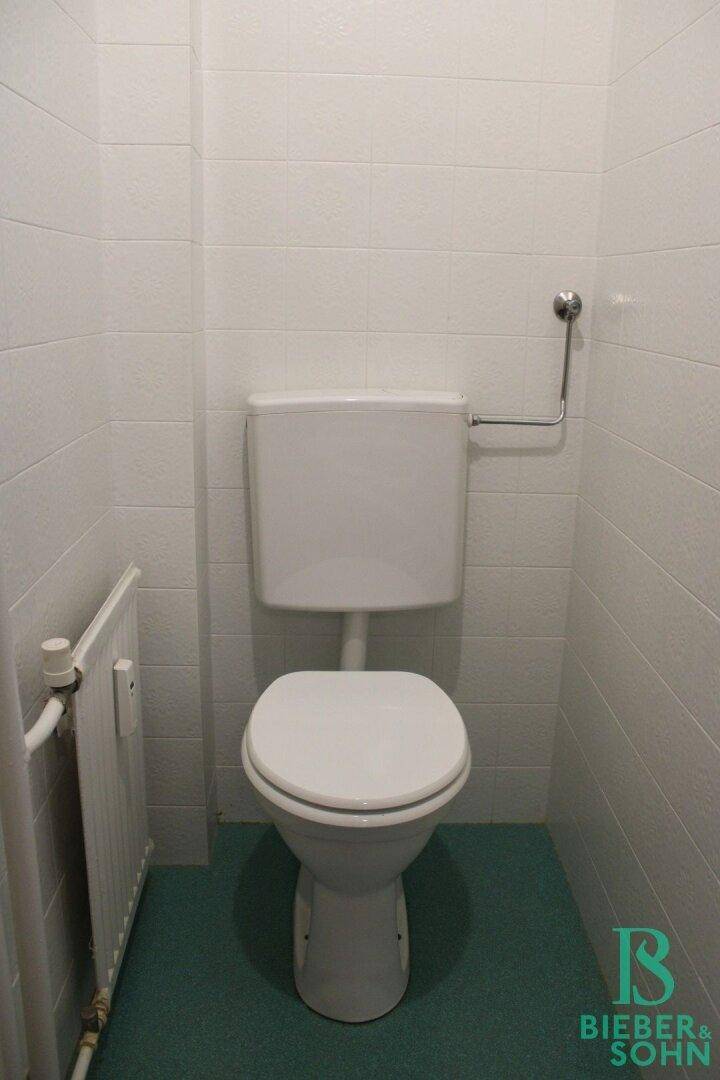 Separate Toilette mit weißer Keramik und weiß-türkisen Fliesen.