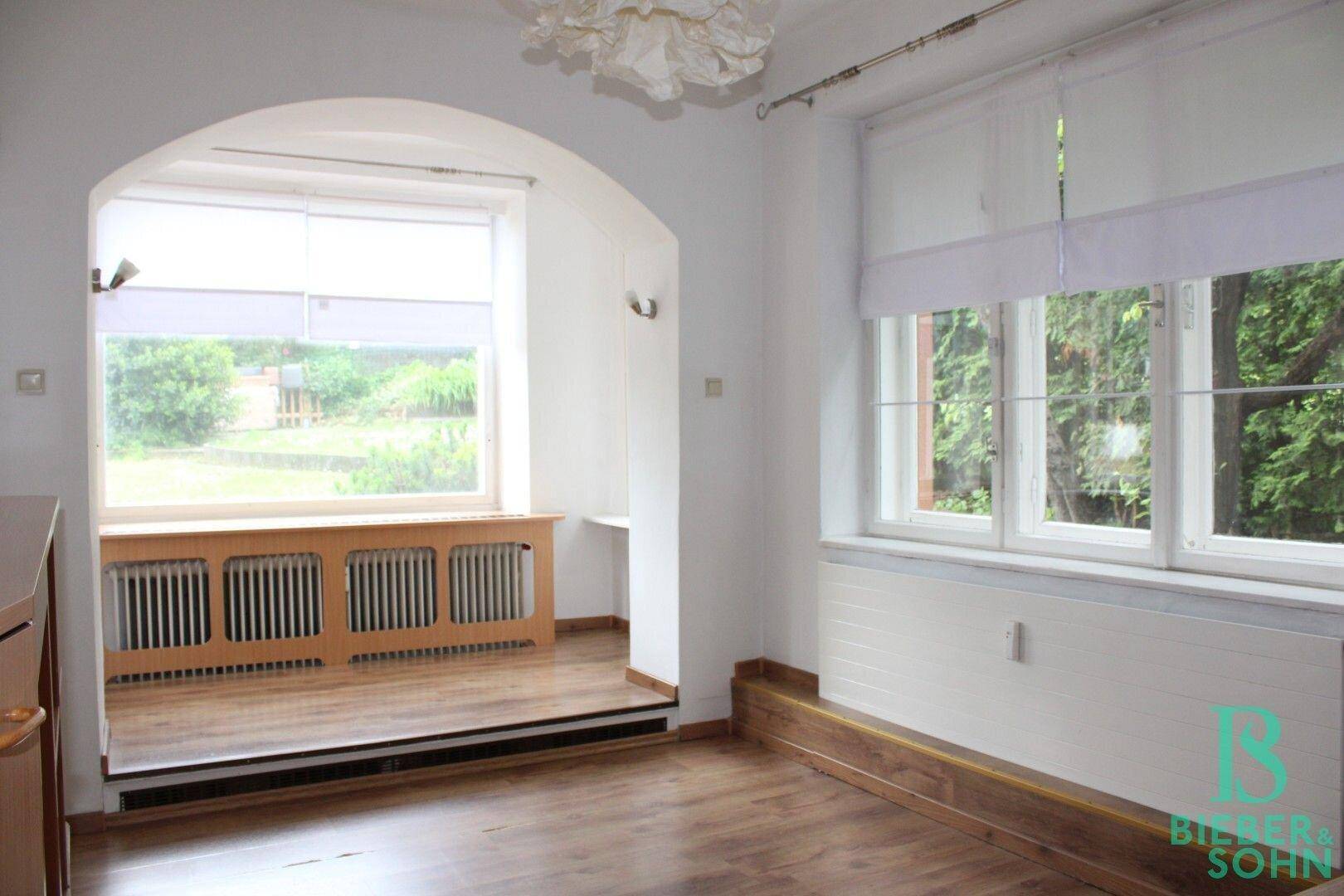 Helles Zimmer mit Holzboden, großem Fenster und Blick in den Garten.