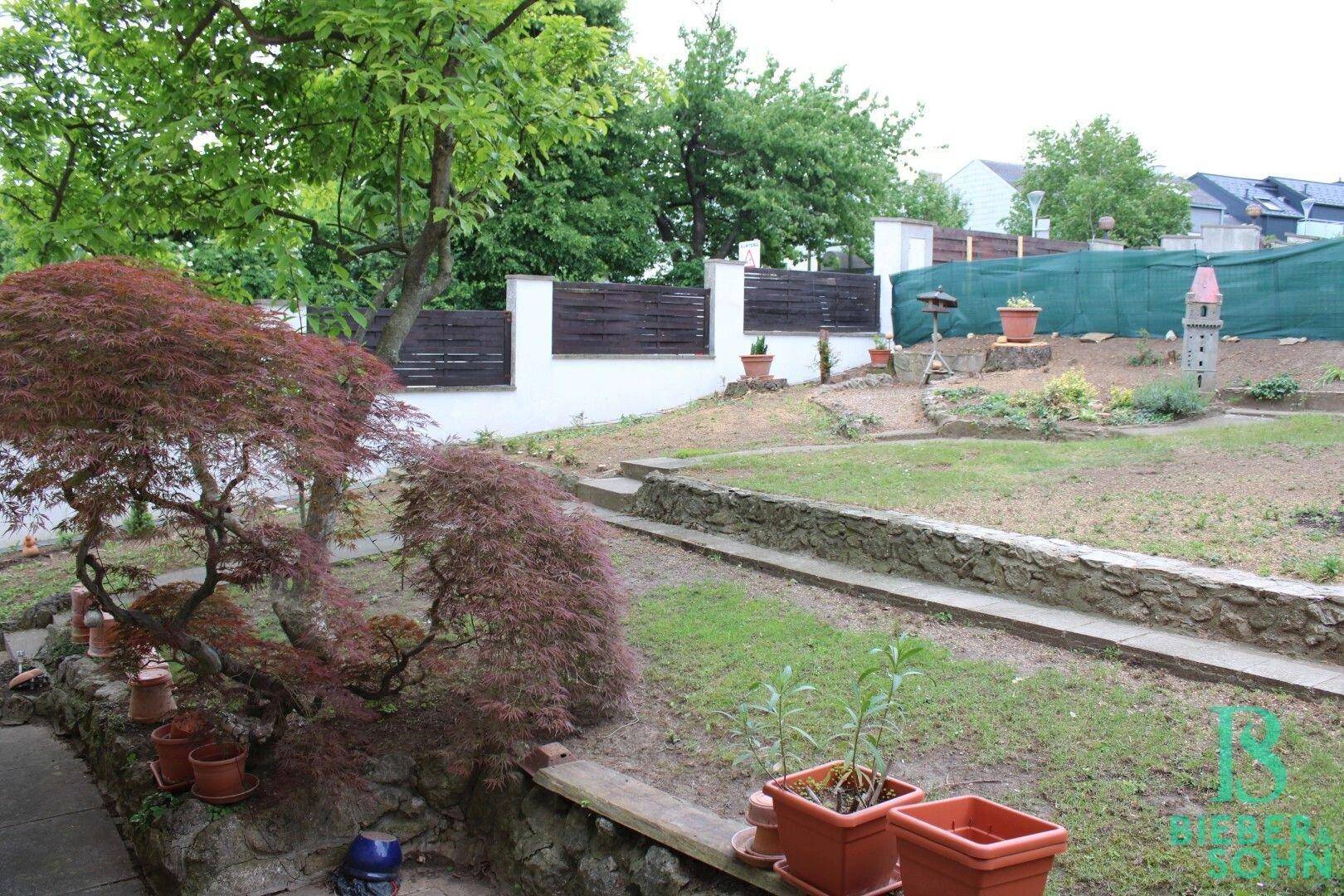 Großer Garten mit Rasenfläche, Bäumen und einem kleinen Gartenhäuschen im Hintergrund.