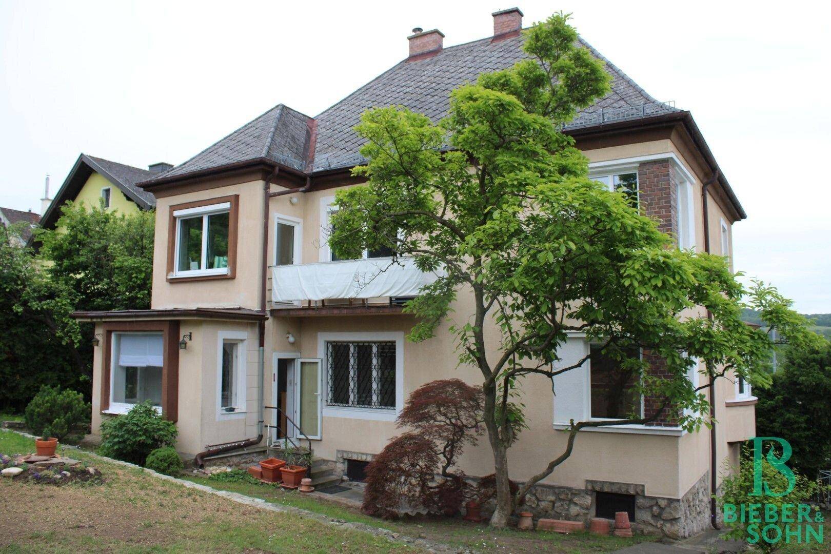 Charmantes Haus mit mehreren Fenstern, Balkon und einem gepflegten Garten.