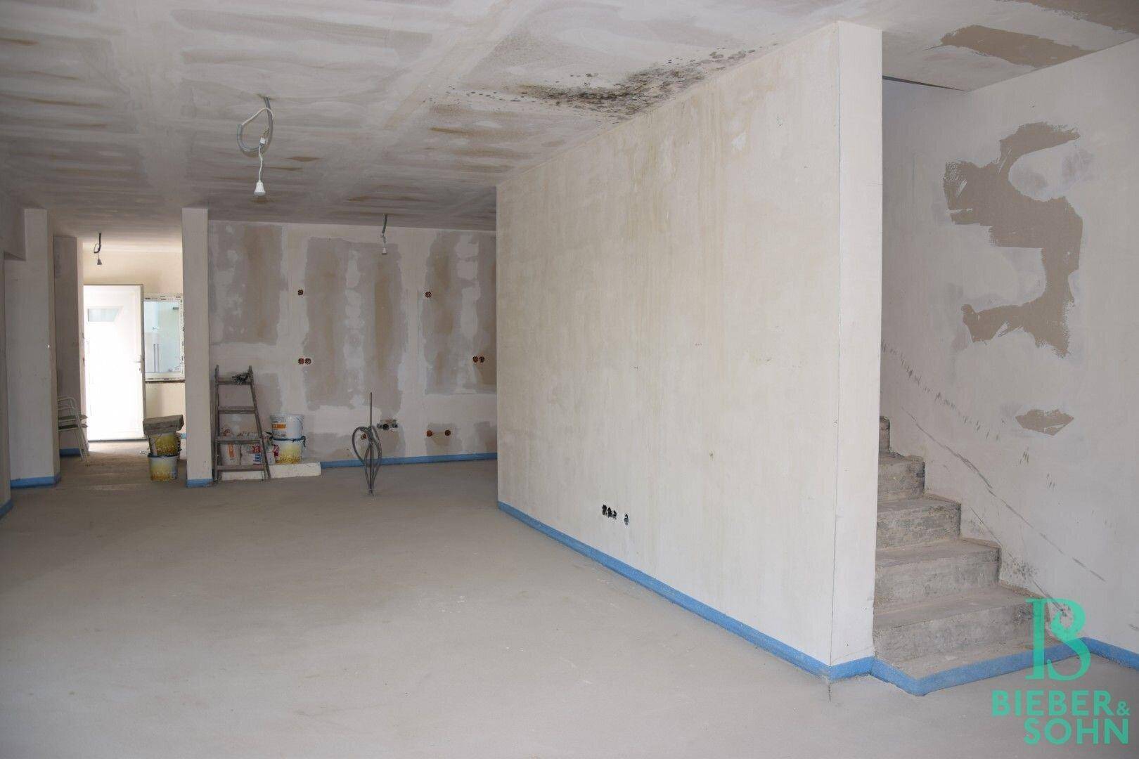 Rohbau-Innenraum mit sichtbarer Treppe und offenem Bereich, der auf den weiteren Ausbau wartet.