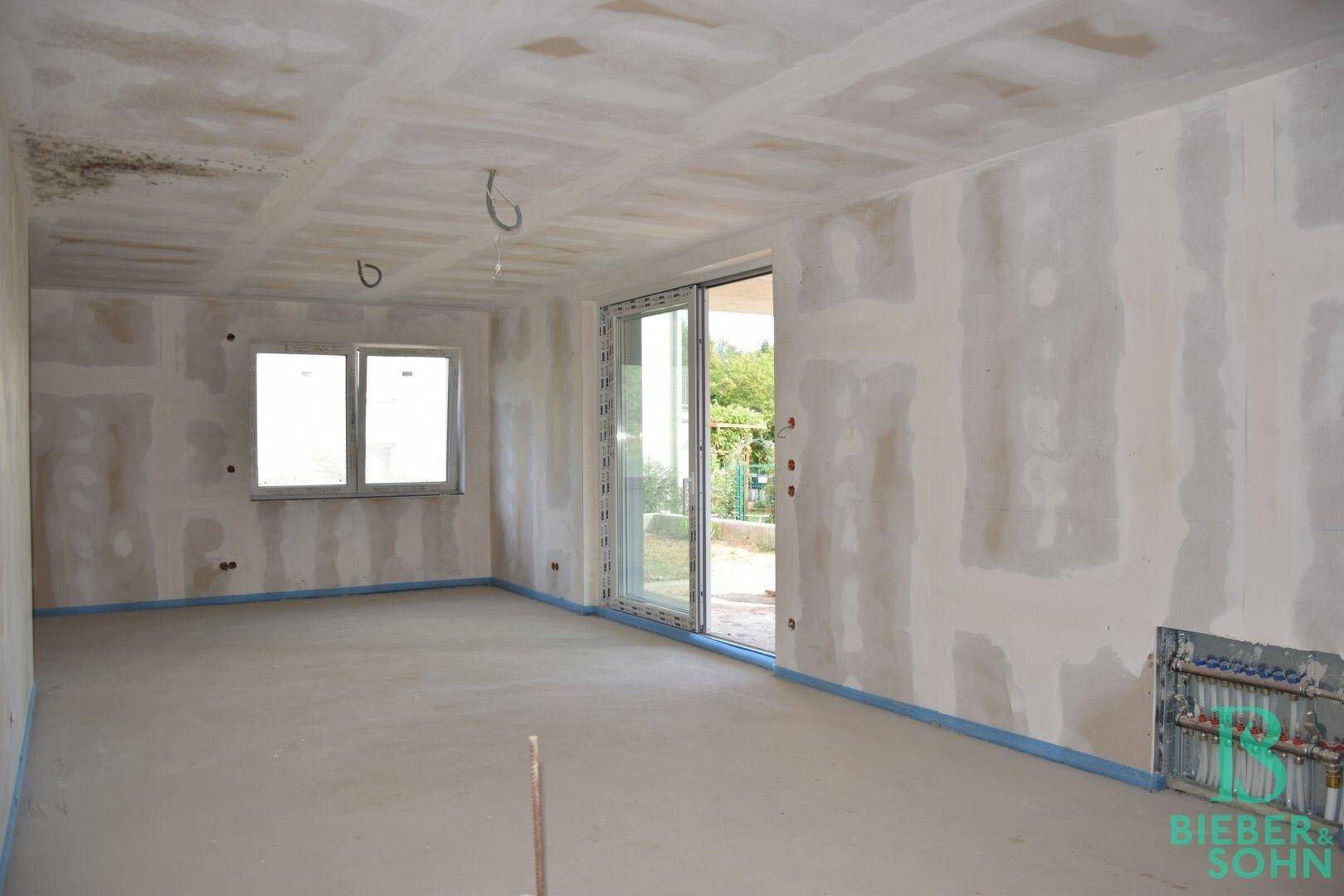 Unfertiger Innenraum mit großen Fenstern und Schiebetür, bereit für den weiteren Ausbau.