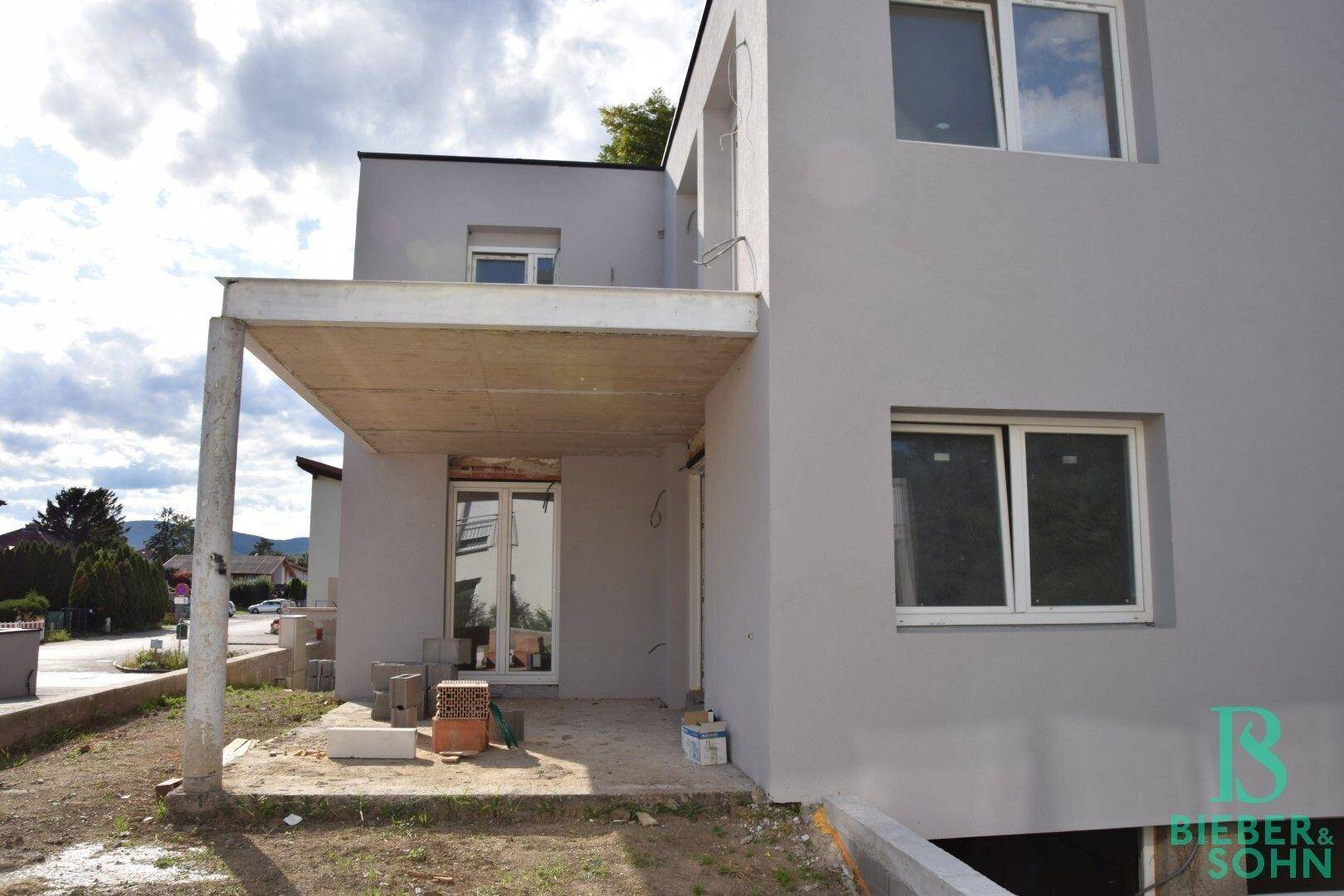 Seitenansicht eines modernen Neubaus mit Rohbau-Balkon und großen Fensterfronten.