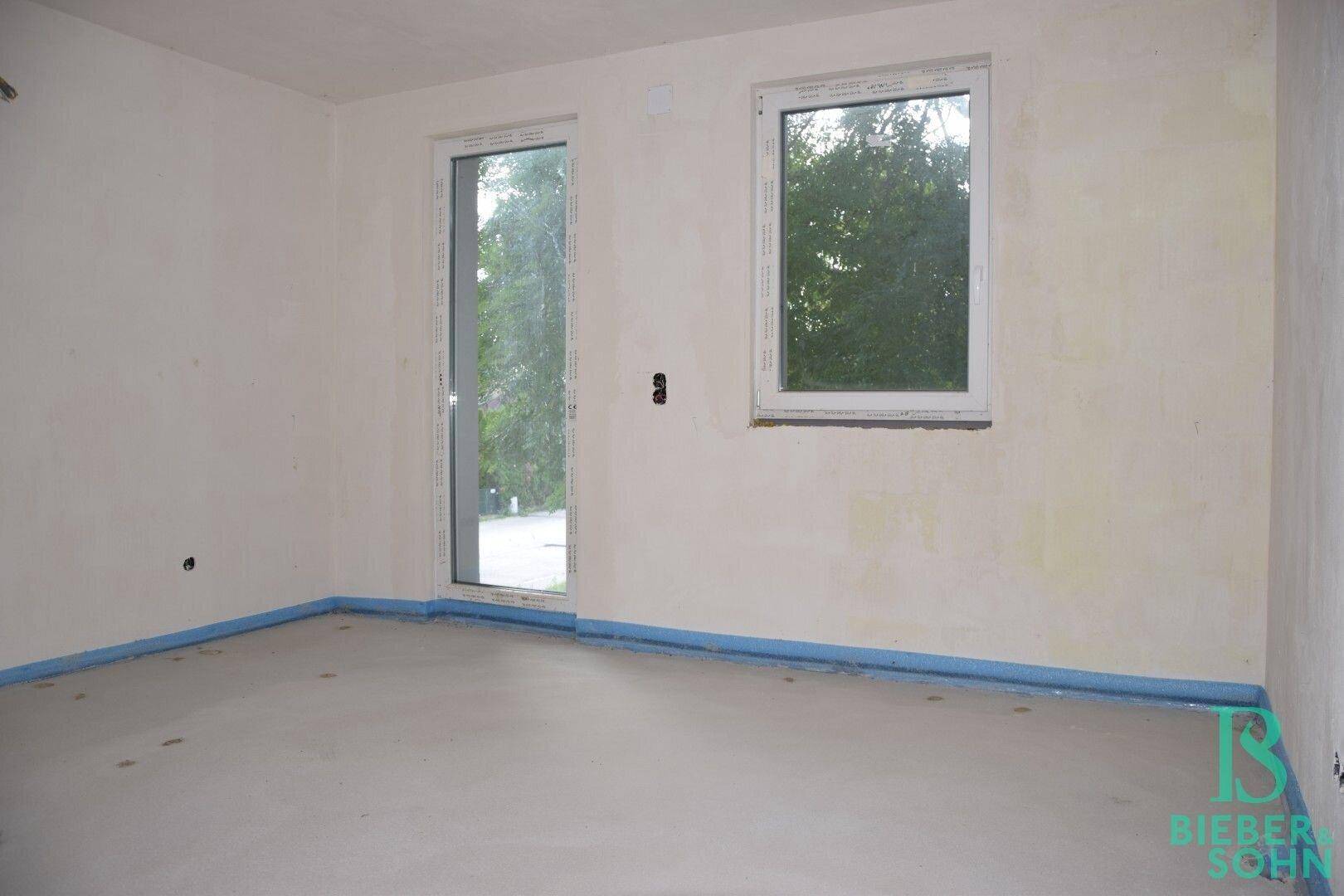 Rohbau-Zimmer mit einem Fenster und einer Tür, die auf den weiteren Innenausbau warten.