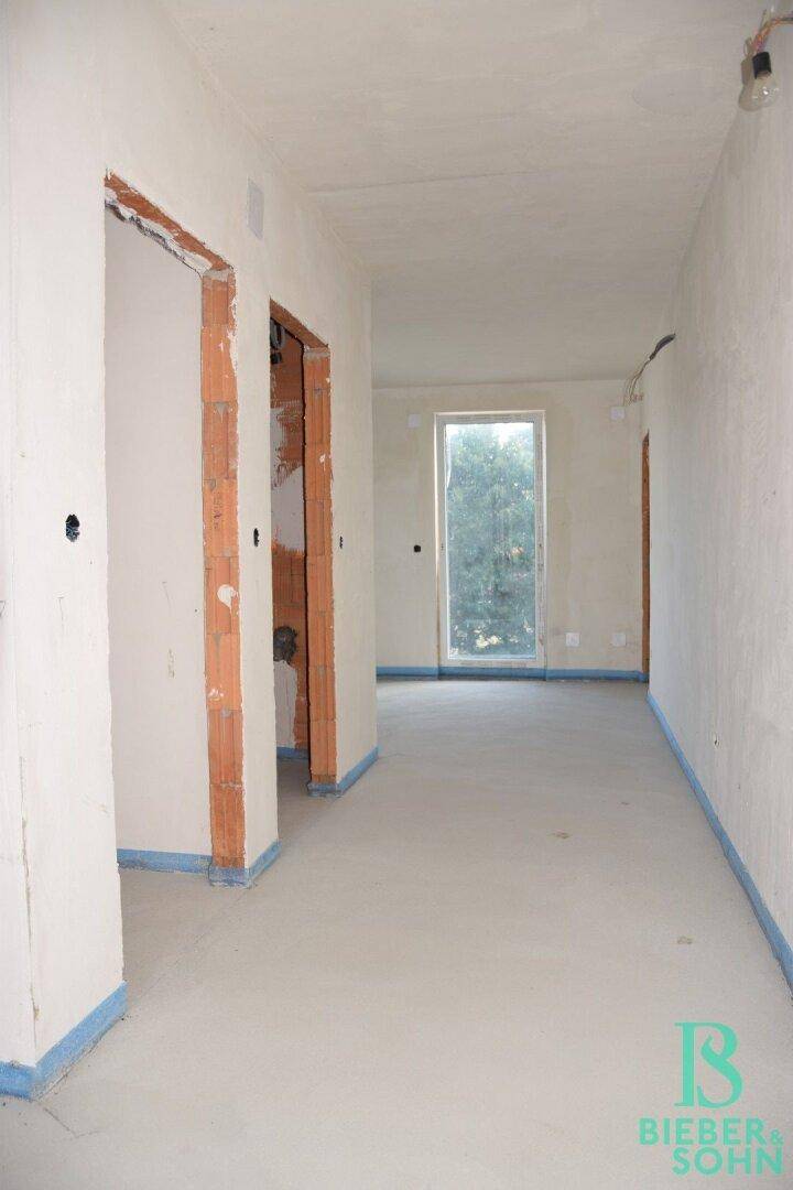 Heller Flur im Rohbau mit einem großen Fenster, das Tageslicht in den Raum bringt.