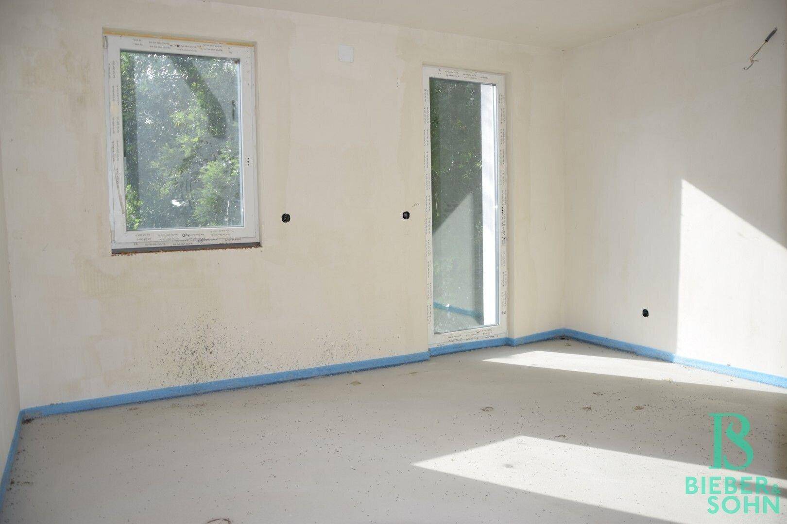 Heller Rohbau-Raum mit Fenster und Tür, der viel Sonnenlicht empfängt und auf Fertigstellung wartet.