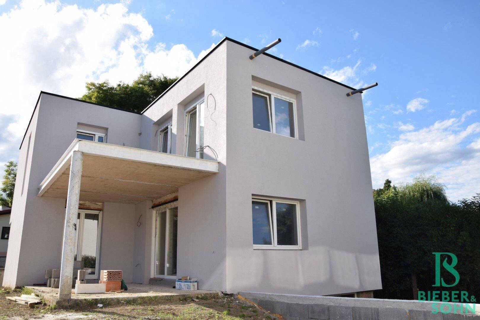 Moderne Hausfassade im Bau mit großen Fenstern und einem zukünftigen Balkonbereich.