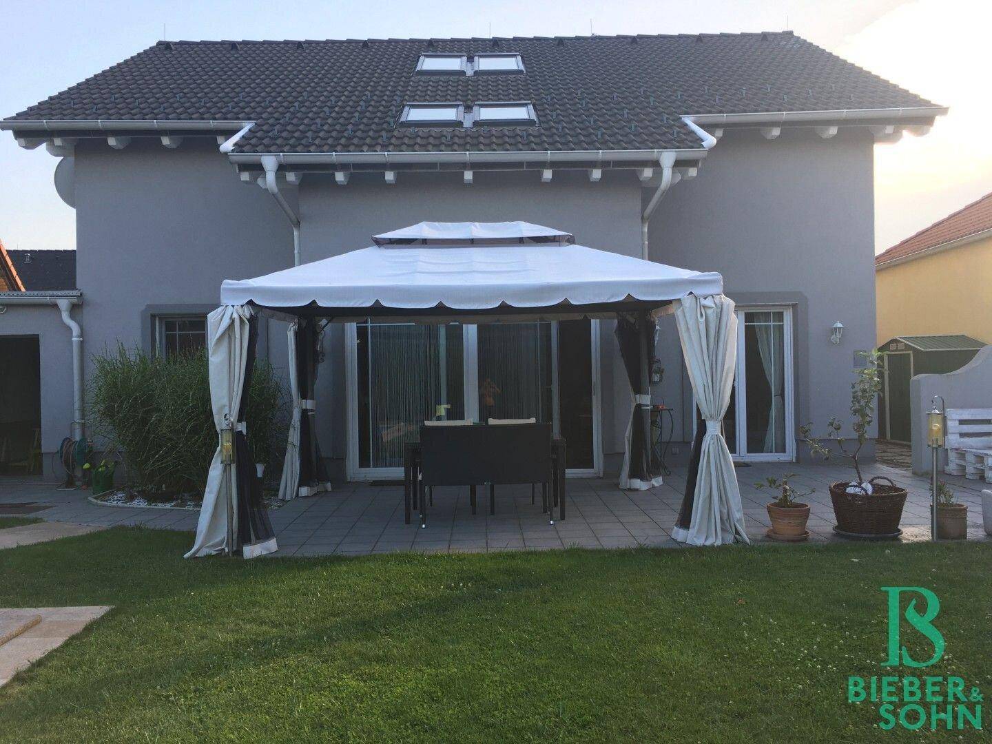 Hinteransicht des Hauses mit überdachter Terrasse, Gartenmöbeln und Rasenfläche.